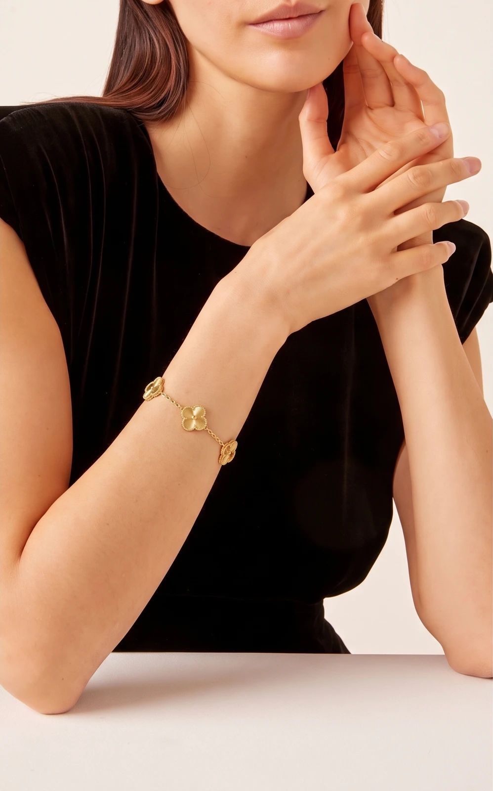 Gold clover bracelet worn on a model’s wrist against a black top