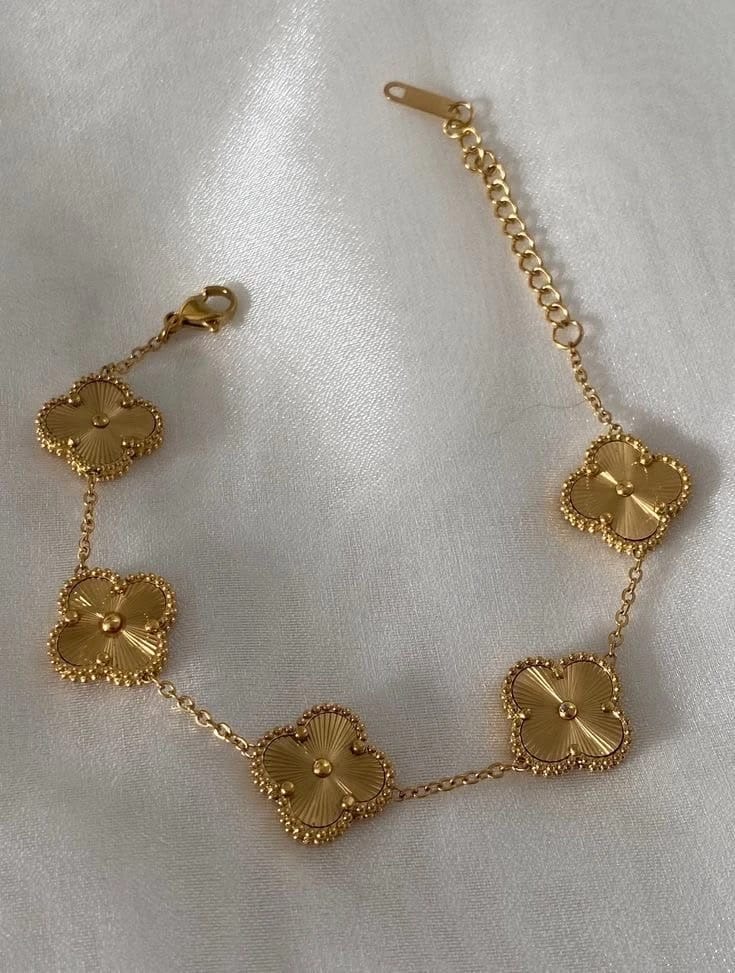Gold bracelet with clover-shaped charms arranged on a white surface