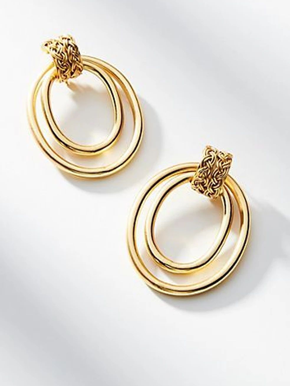 Gold hoop earrings with layered circular details arranged on white