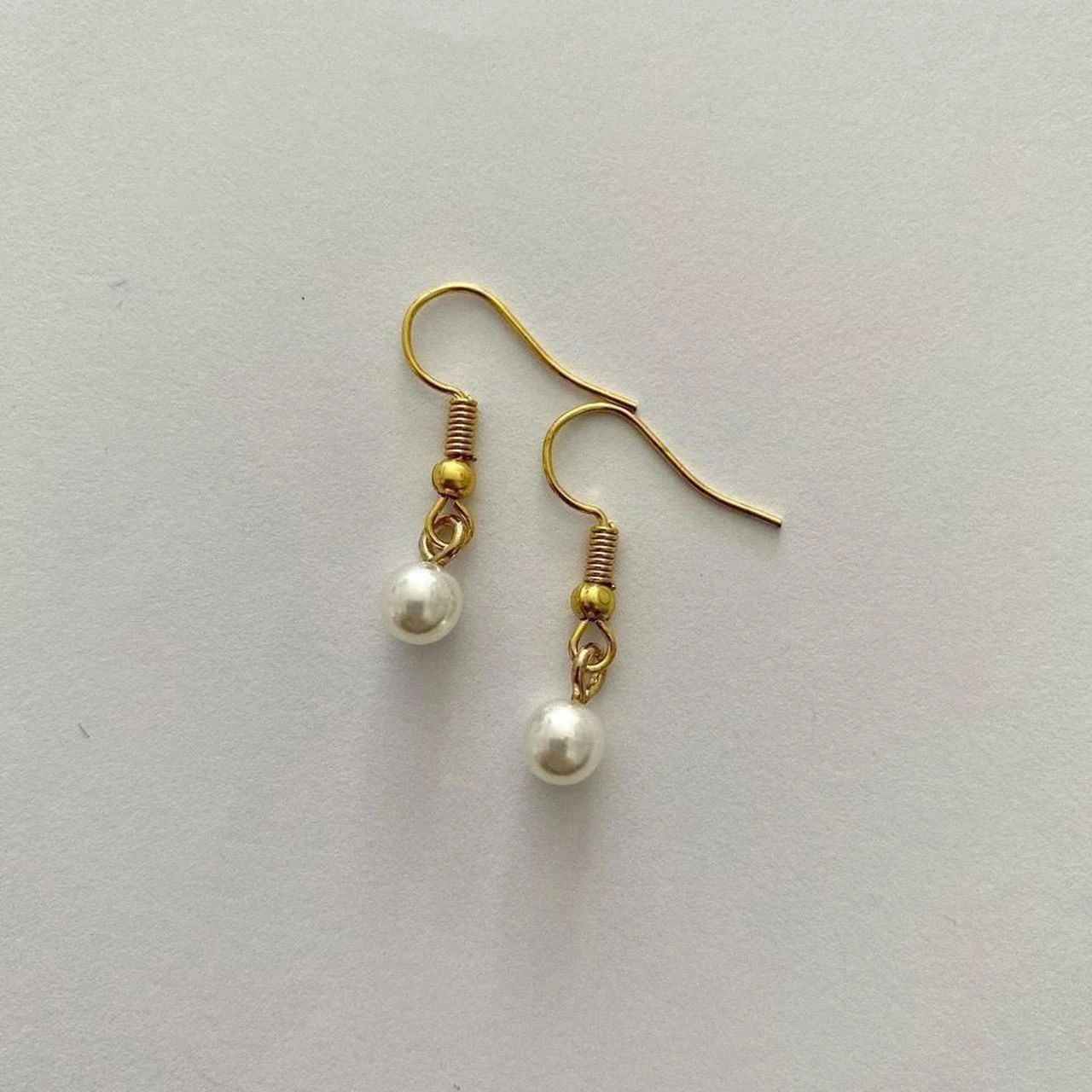 Gold hook earrings with white pearl drops on a textured light surface