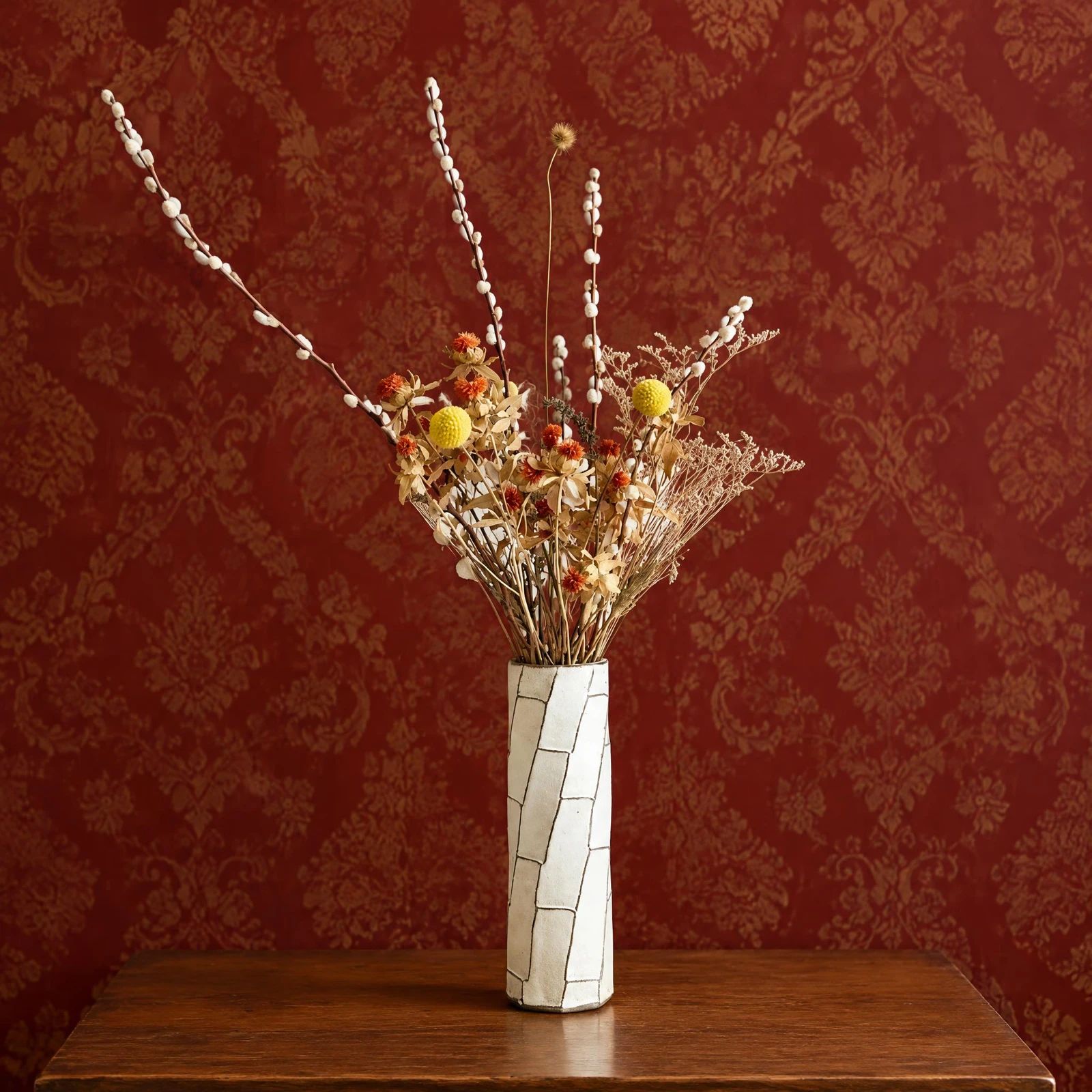 Vase of dried flowers styled against red patterned wallpaper