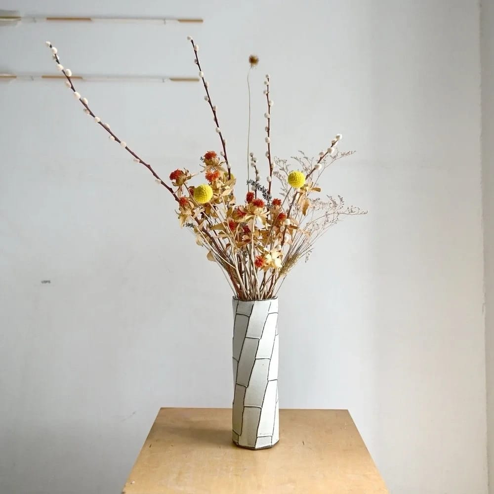 Clear vase with dried flowers on a table against a plain wall