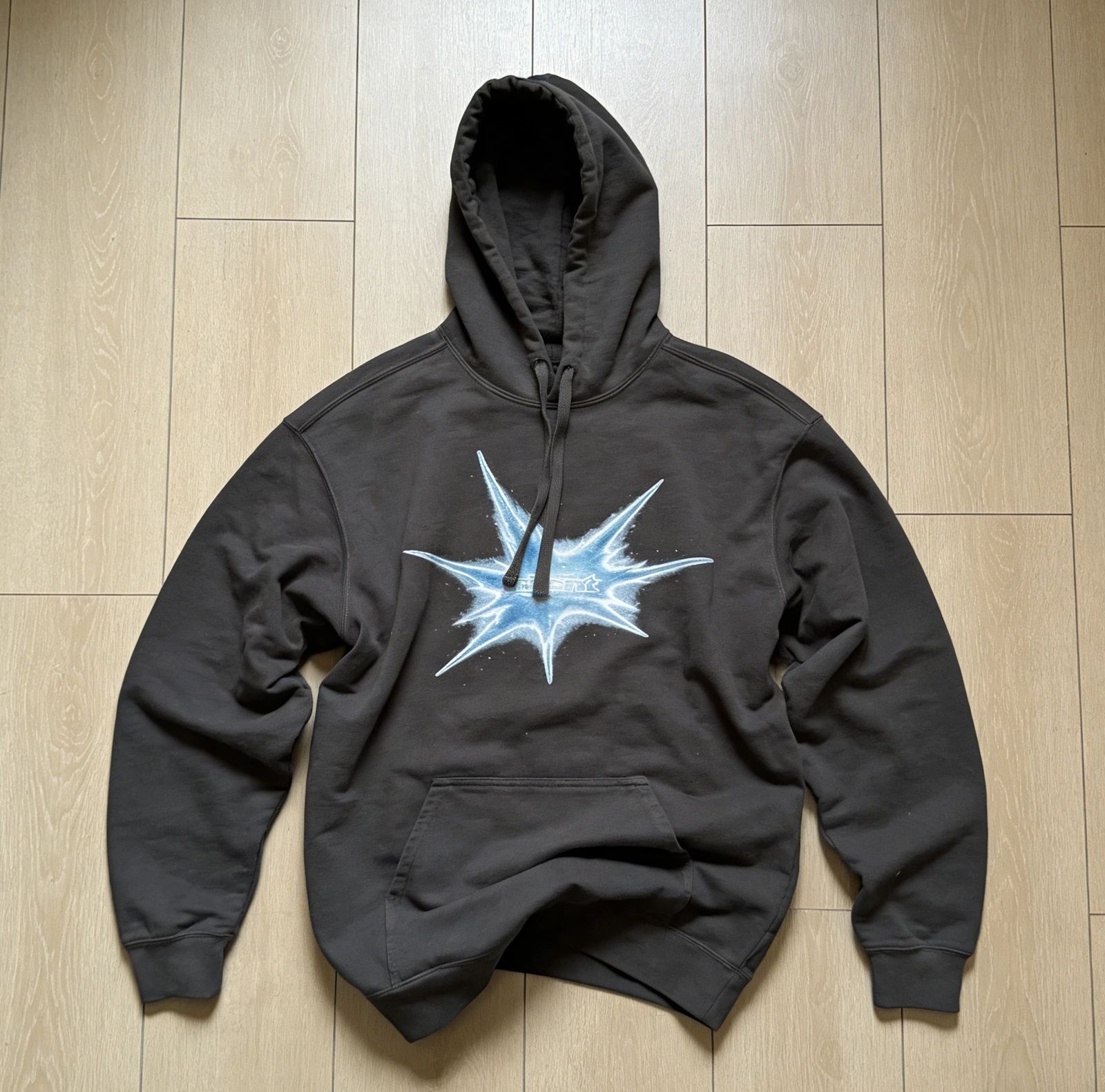 Black hoodie with a blue-and-white chest graphic laid flat on a wood floor