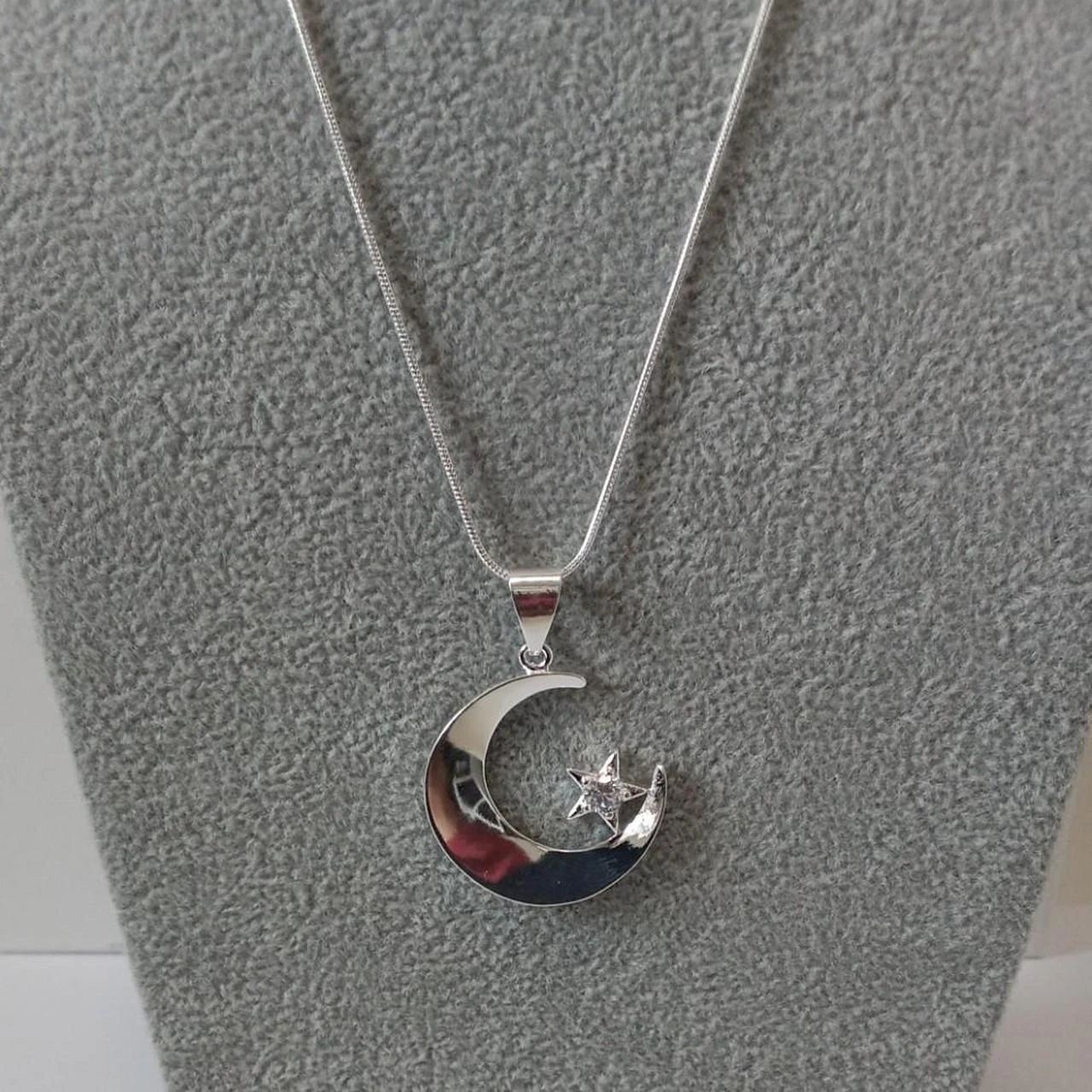 Silver crescent-moon and star pendant on a textured gray surface