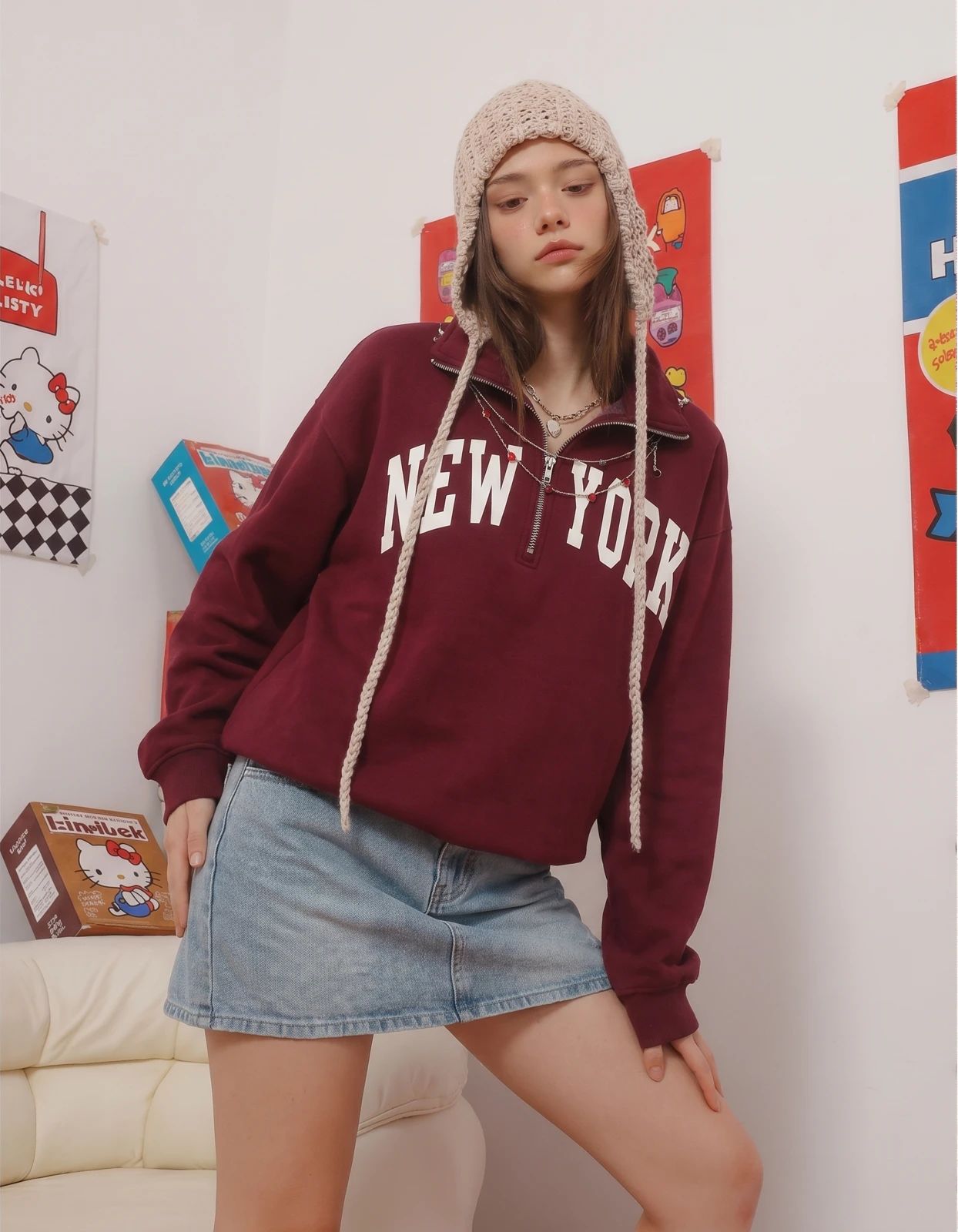 Model wearing a burgundy New York hoodie and denim skirt in a casual room