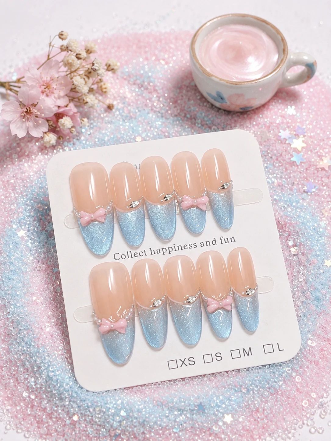 Nude press-on nails styled with pink blossoms on a glittery pastel surface