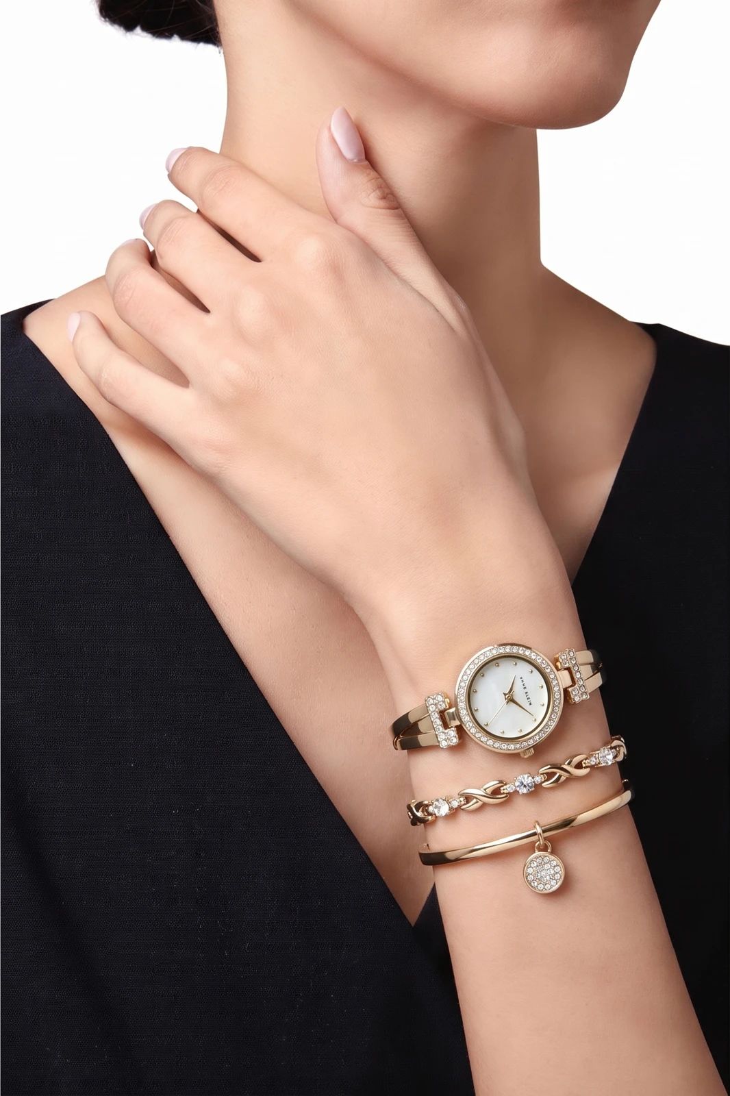 Gold wristwatch and bracelet worn together on a model’s wrist against a black sleeve