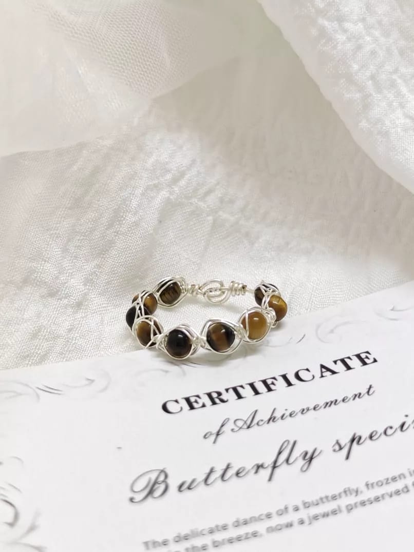 Before Snappyit Jewelry Retouch — seller photo of a wire-wrapped tiger's eye ring on a certificate card with cluttered background