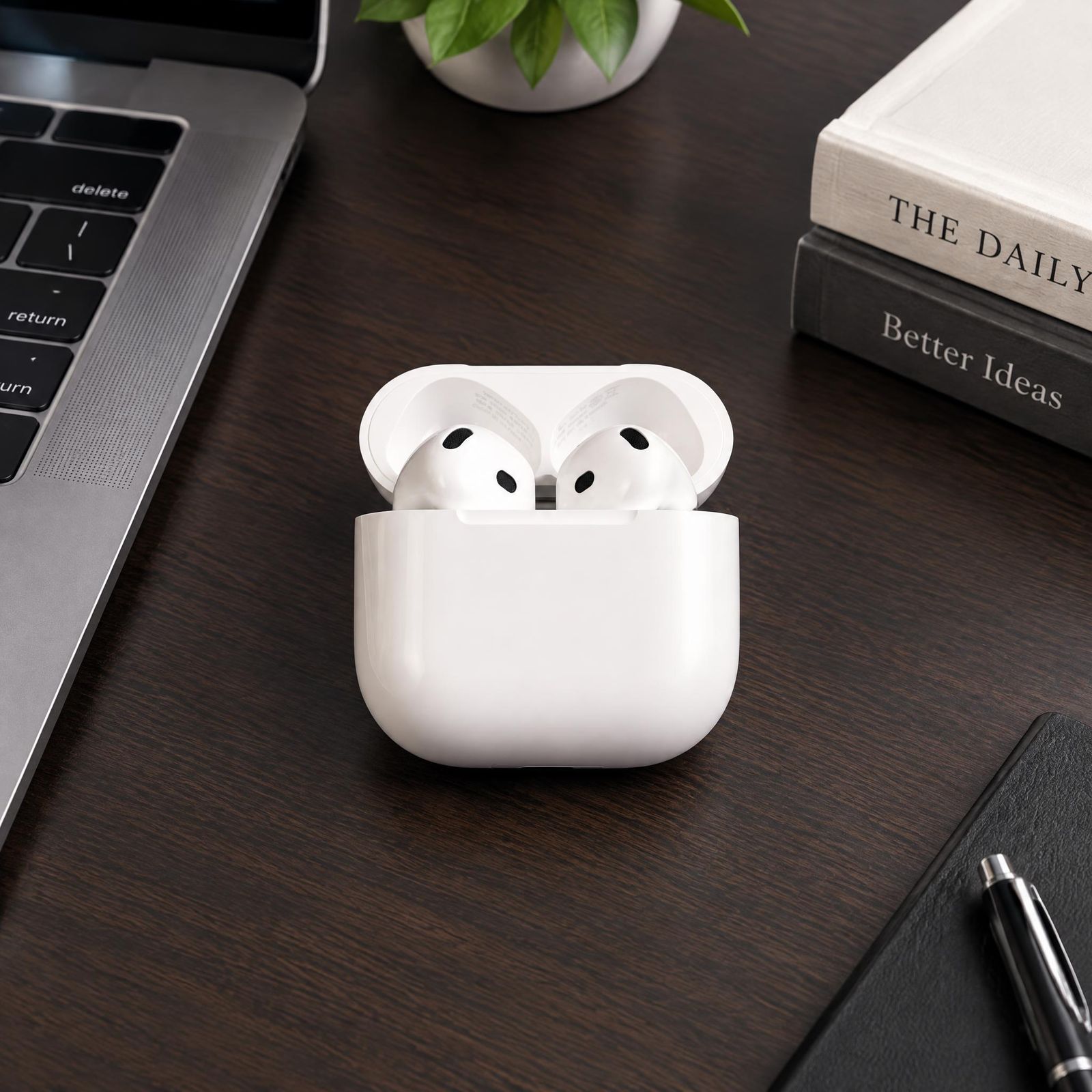 Wireless earbuds on a dark wooden desk beside a laptop and books