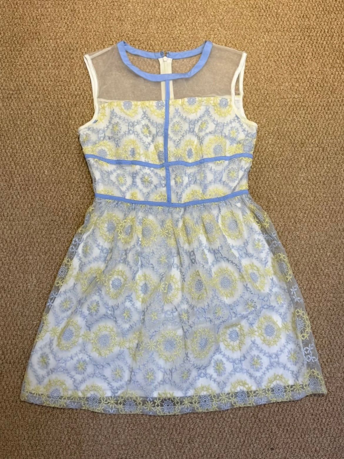 Original phone photo of a blue and yellow embroidered dress laid on a brown textured surface