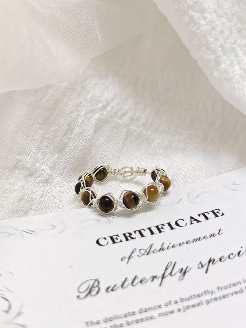 Before Snappyit Jewelry Retouch — seller photo of a wire-wrapped tiger's eye ring on a certificate card with cluttered background