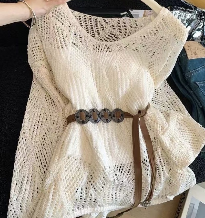 Cream knit top gathered with a belt and folded against a cluttered background