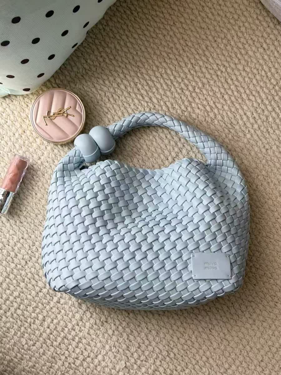 The source photo of the woven handbag on a knit rug, with a pouch, a compact and a lipstick in frame
