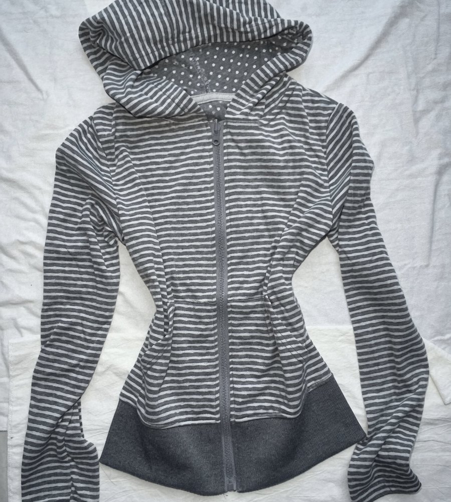 Grey and white striped zip hoodie laid flat on a bedsheet, hood open showing the polka dot lining