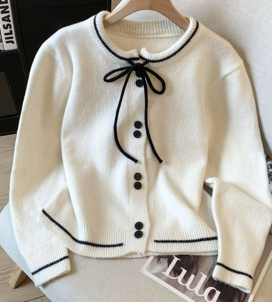 White knit cardigan with black ties draped over a cream armchair, phone photo