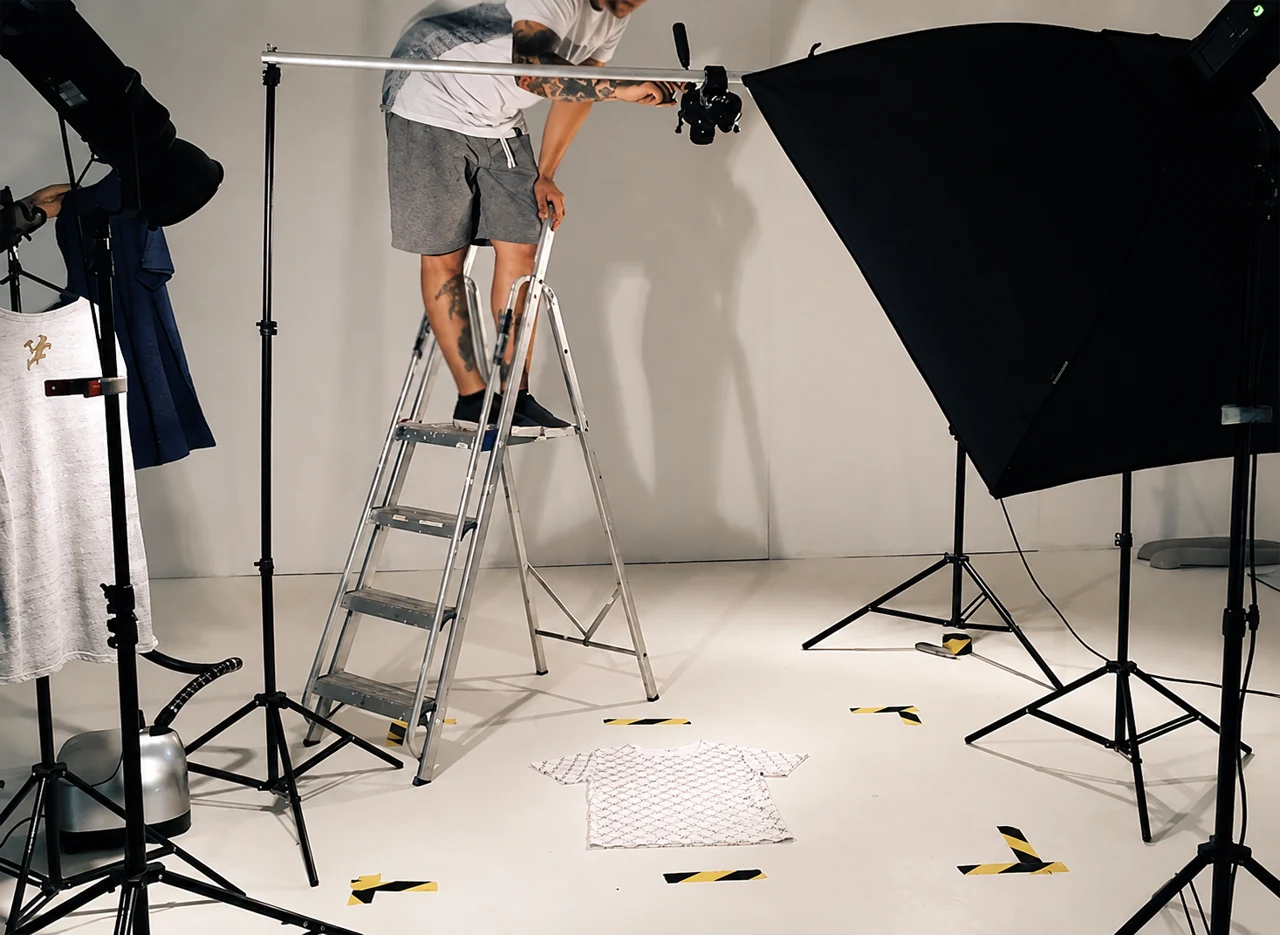 Traditional flat lay photography setup with an overhead camera, lighting, garment, and floor position markers