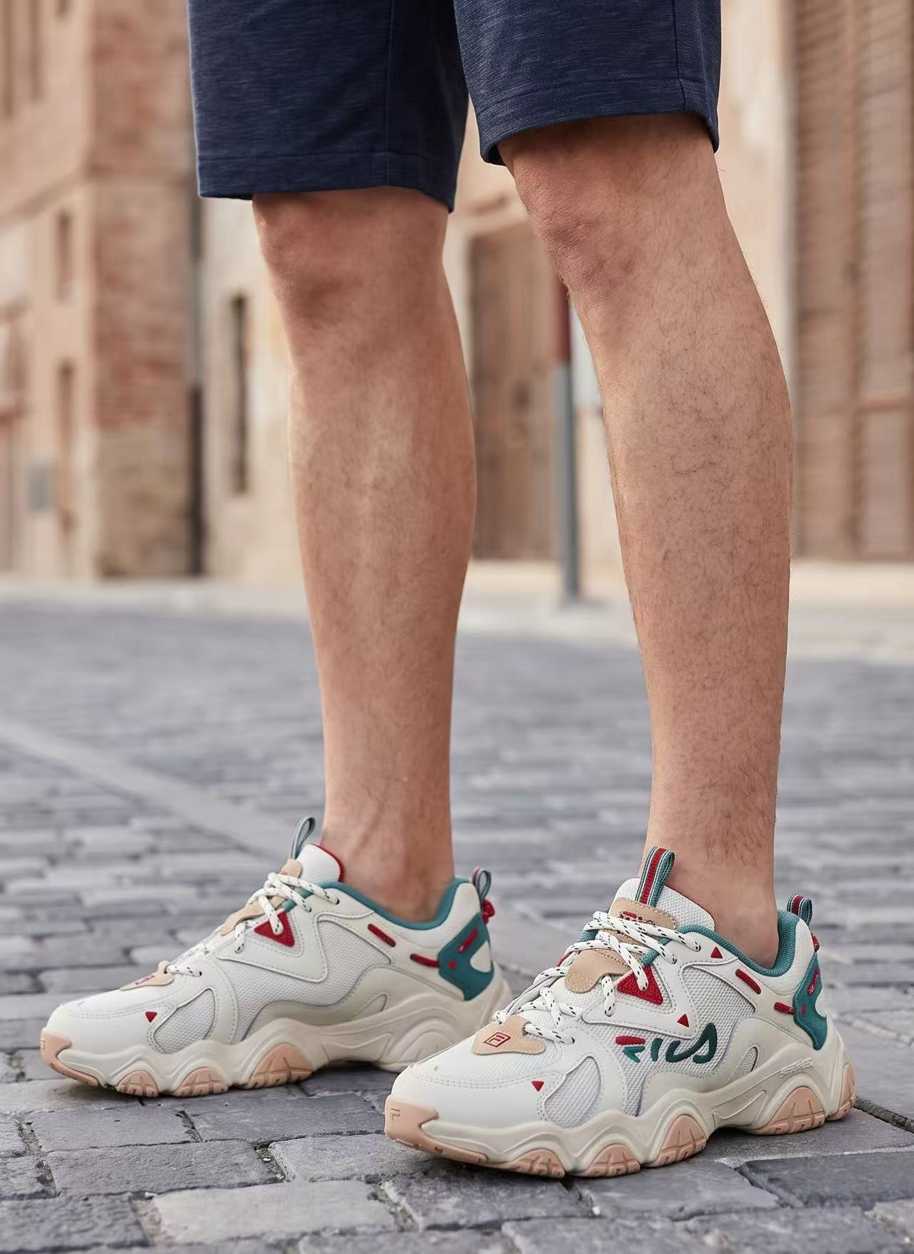 The FILA trainer worn by an AI-generated model, framed from the knees down on a cobbled street