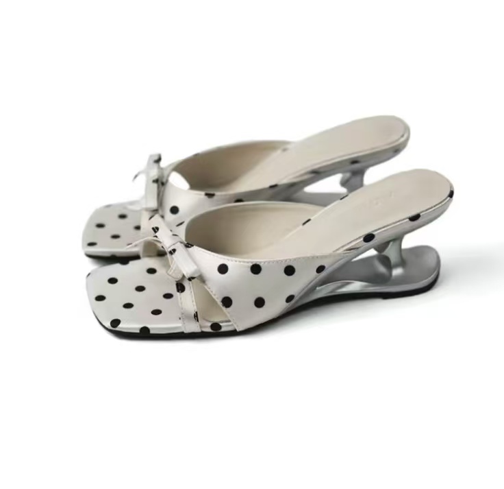 White polka-dot mule with a square open toe, a bow at the strap and a sculpted chrome heel