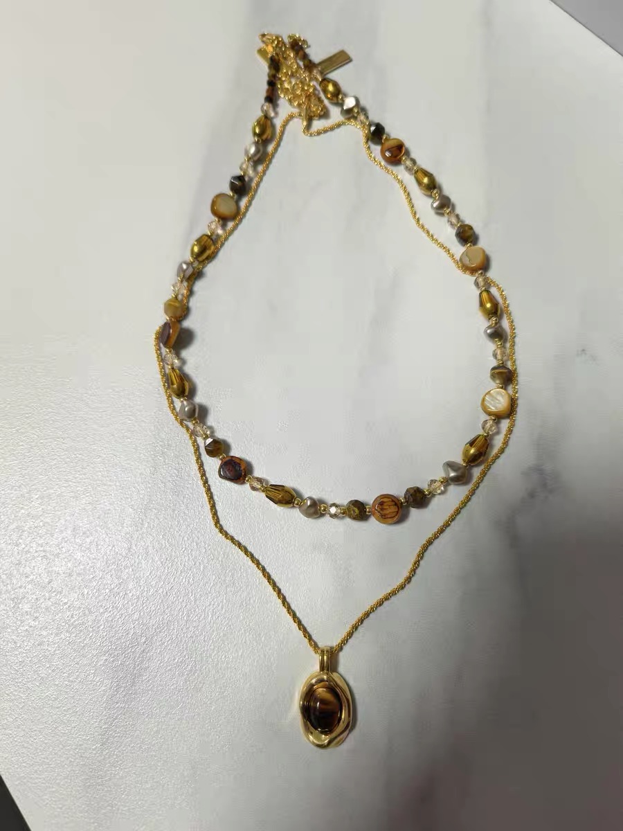 Raw photo: amber and tiger-eye double-layer necklace on a marble-texture desk
