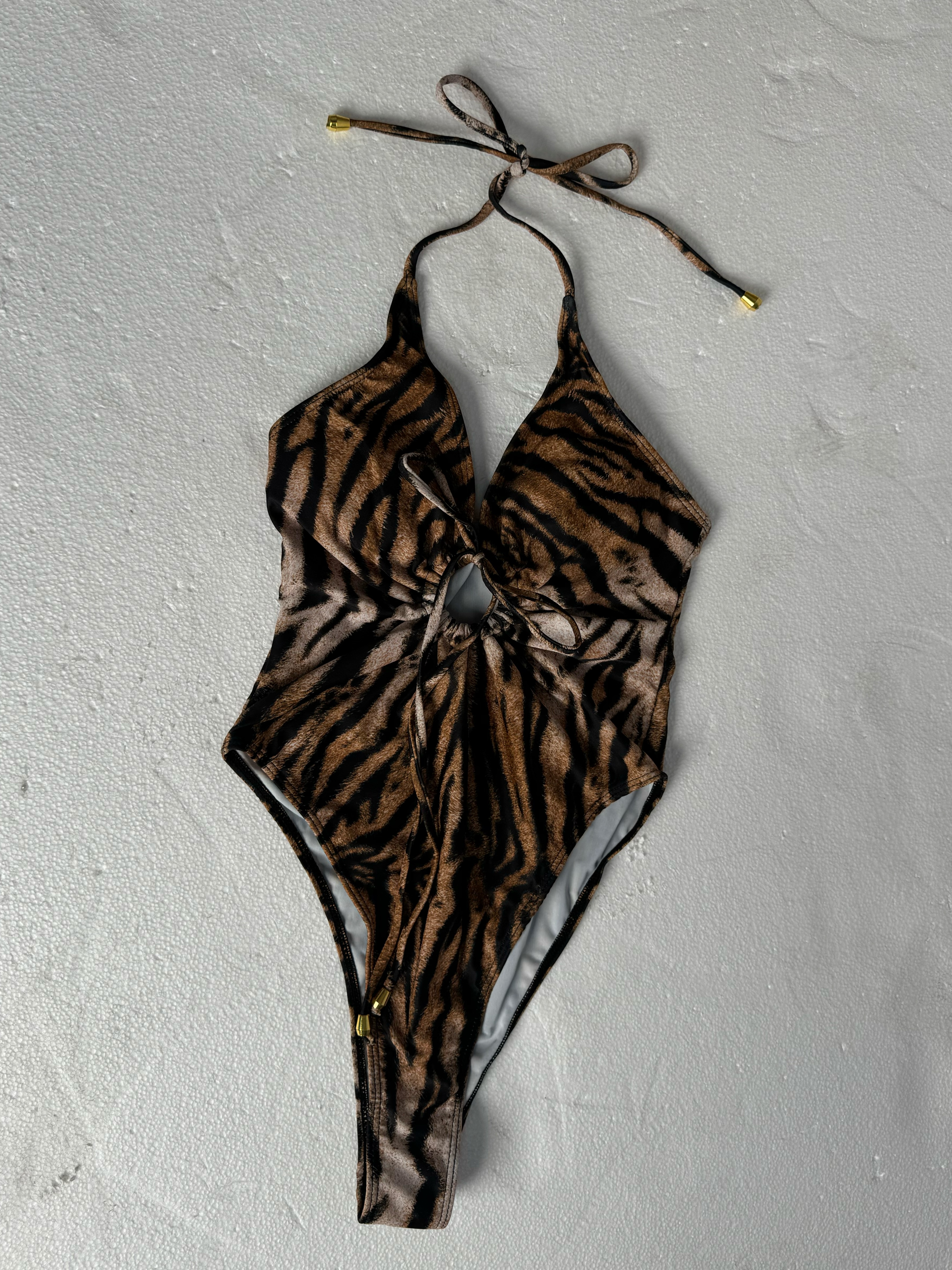 Tiger-print halter one-piece swimsuit raw flat-lay on grey concrete with wrinkled straps and unstructured cup shape — typical supplier file before AI ghost mannequin