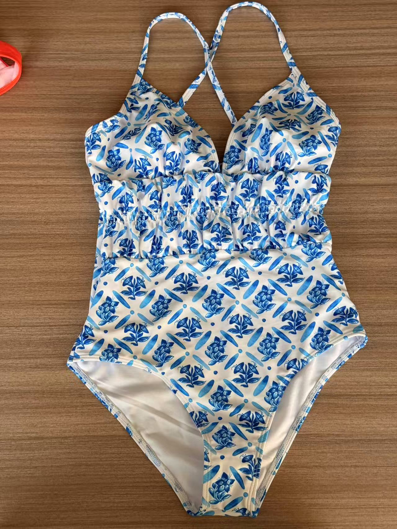 Blue Mediterranean tile-print one-piece swimsuit raw phone flat-lay on dark wooden floor — typical supplier-provided photo before AI on-body generation